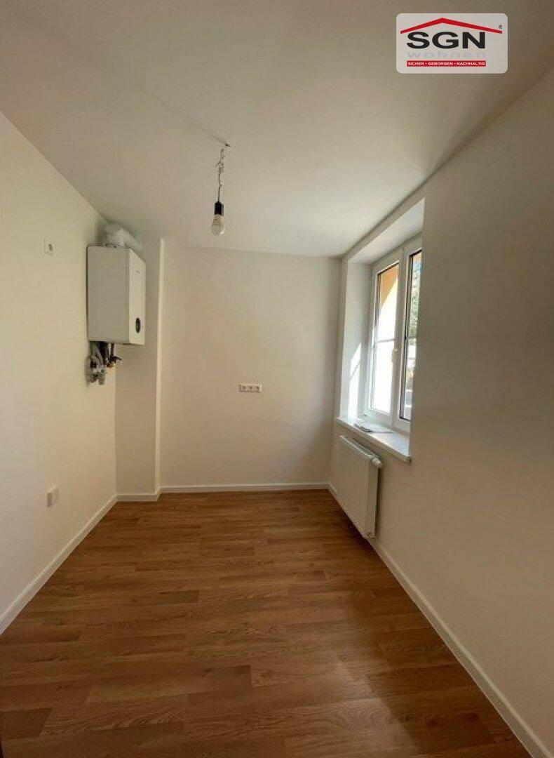 Kleines Zimmer mit Holzfußboden, Fenster und Heizkörper, ideal als Schlaf- oder Arbeitszimmer.