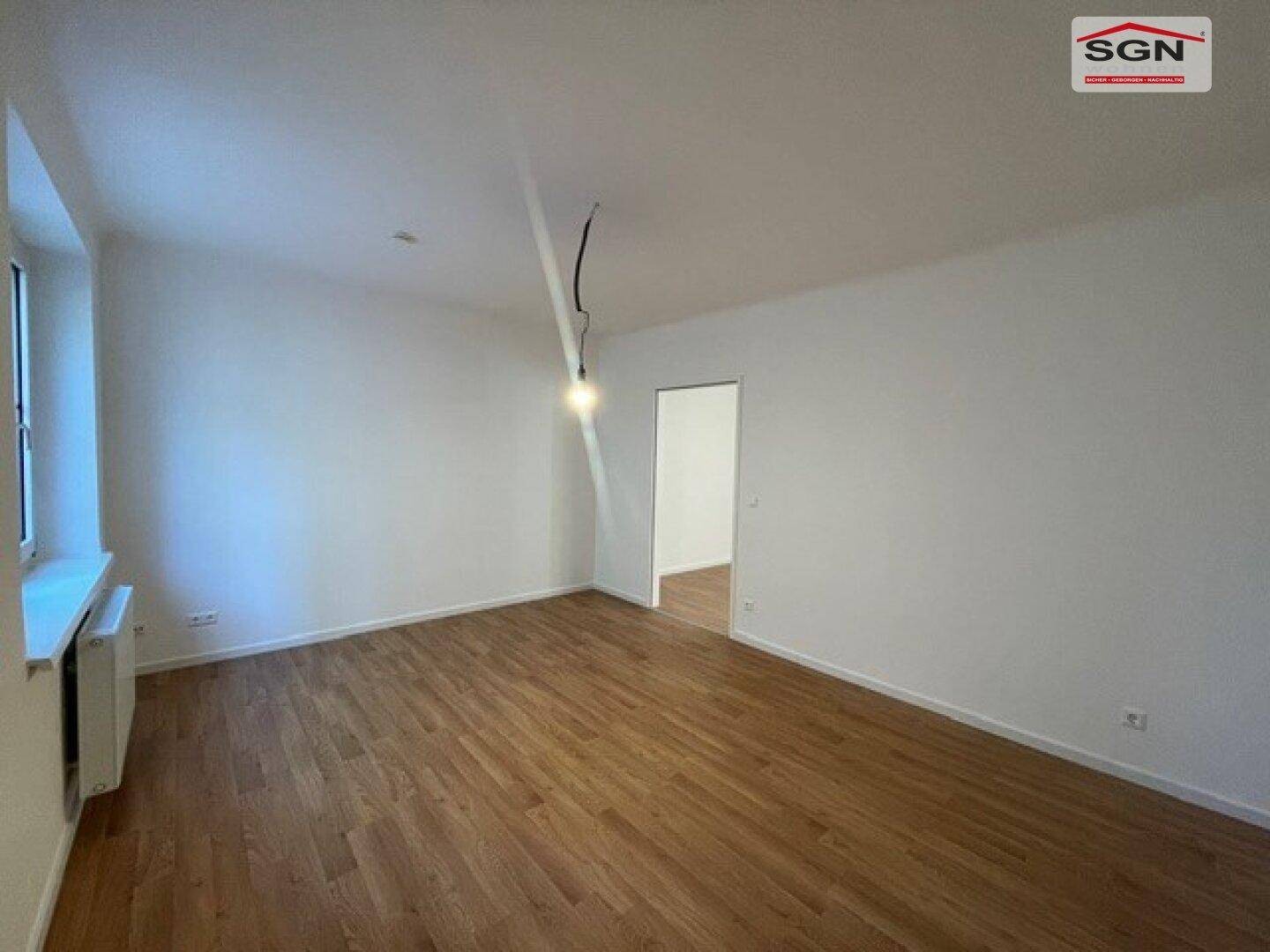 Helles Wohnzimmer mit Holzfußboden und weiß gestrichenen Wänden, bereit zur individuellen Gestaltung.