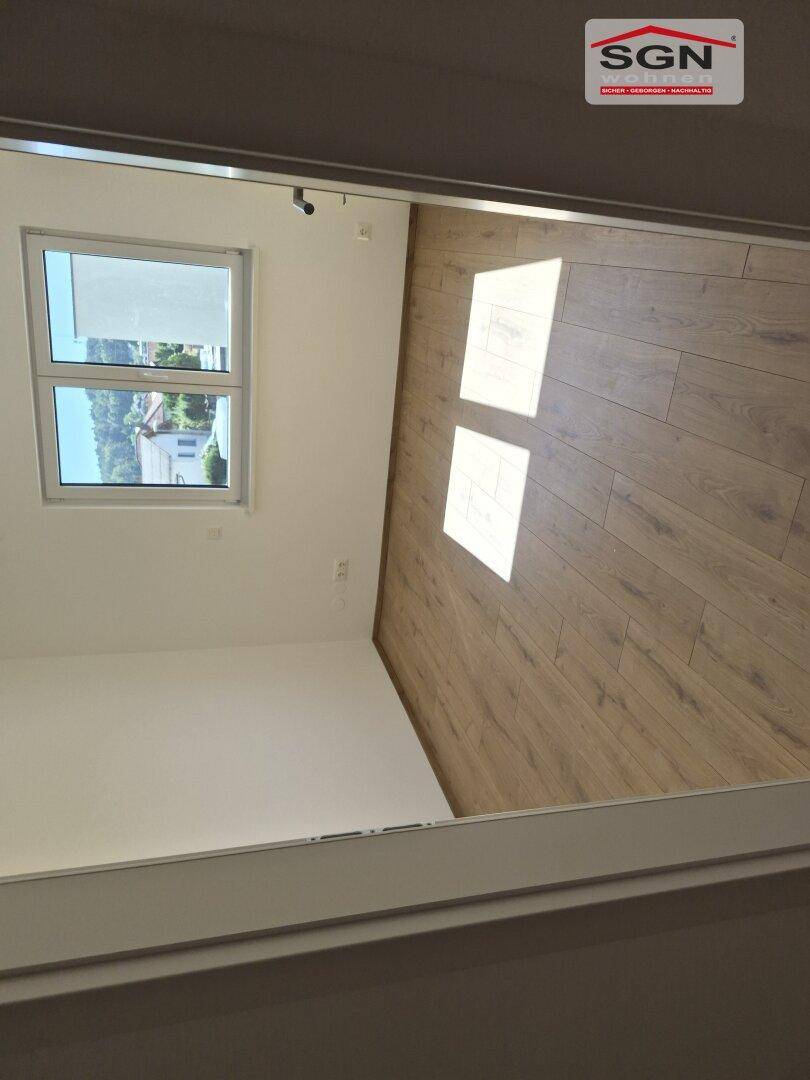 Leeres Zimmer mit hellem Laminatboden und einem Fenster, das den Raum mit natürlichem Licht erfüllt.
