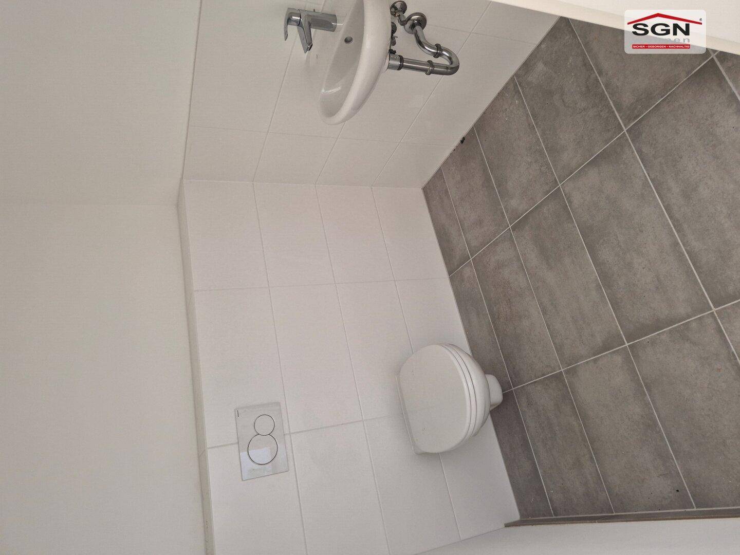 Funktionales Gäste-WC mit wandhängender Toilette, Einzelwaschbecken und modernen Fliesen an Wänden und Boden.