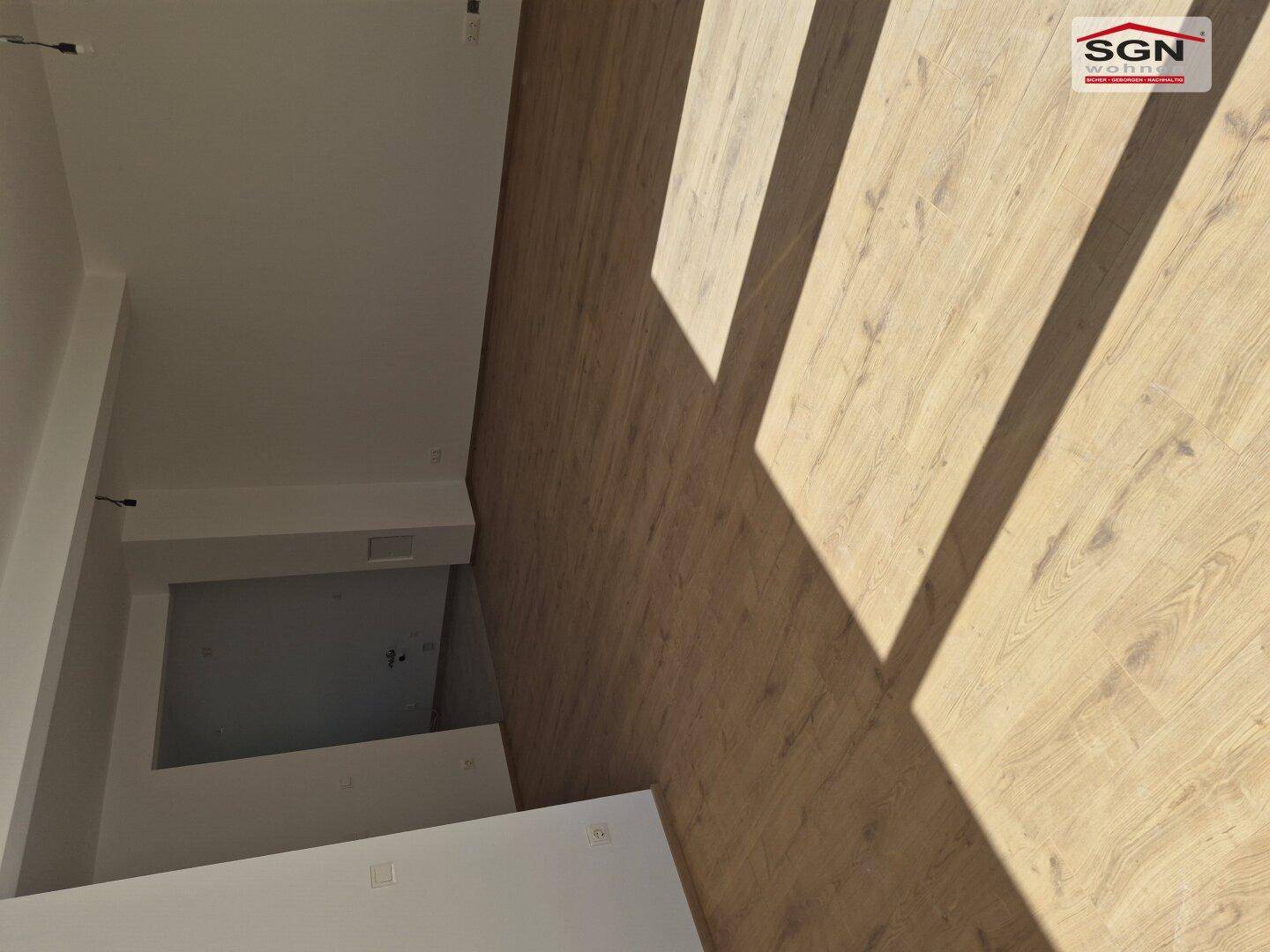 Geräumiger, heller Raum mit Laminatboden, durchflutet von Sonnenlicht, das interessante Schattenmuster wirft.