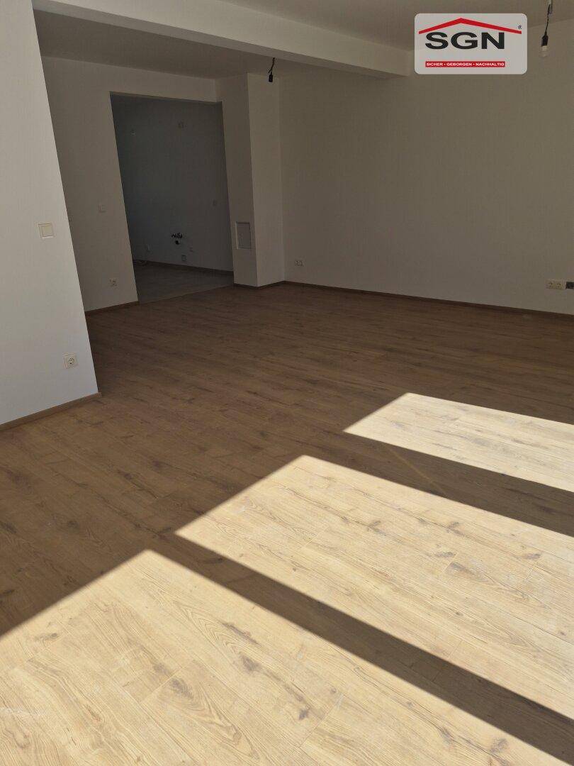 Geräumiger, heller Raum mit Laminatboden und offenem Zugang zu einem weiteren Bereich.