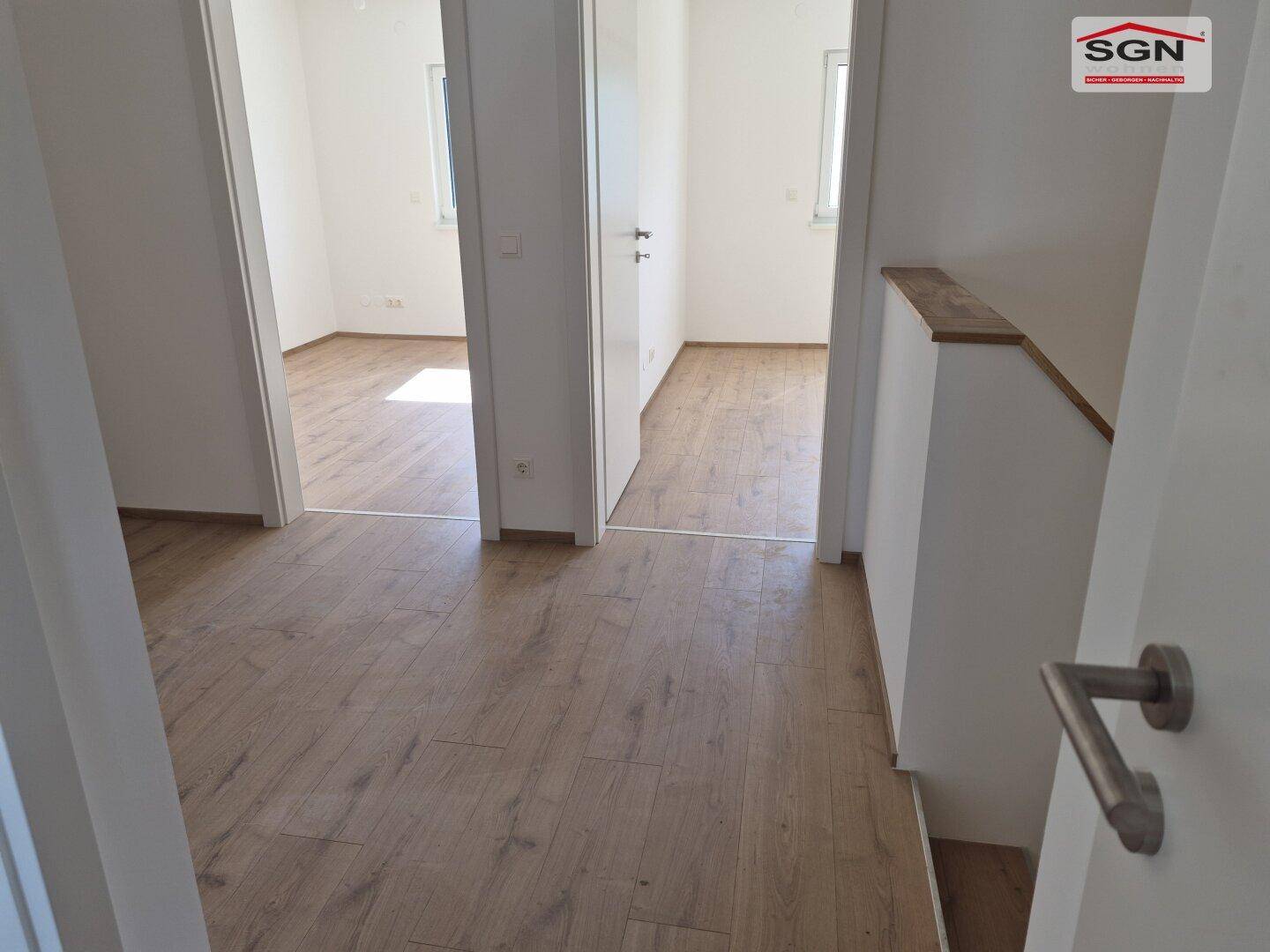 Heller Flur mit Laminatboden, der zu verschiedenen Zimmern und einer Treppe führt.