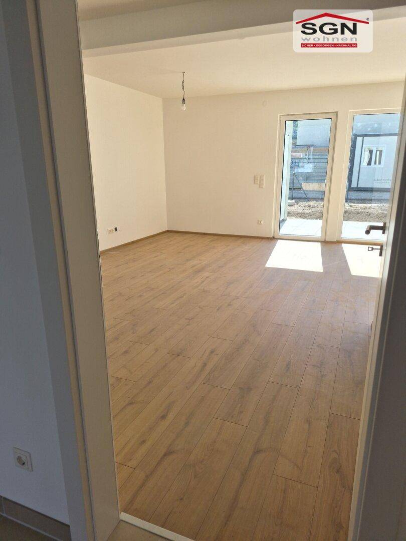Helles Wohnzimmer mit Laminatboden und großen Glastüren, die viel Tageslicht hereinlassen.