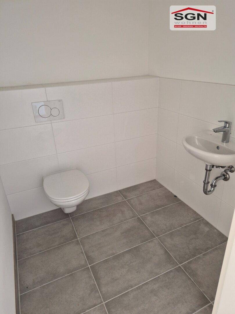 Modernes Gäste-WC mit Wand-WC, Waschbecken und grauen Bodenfliesen.