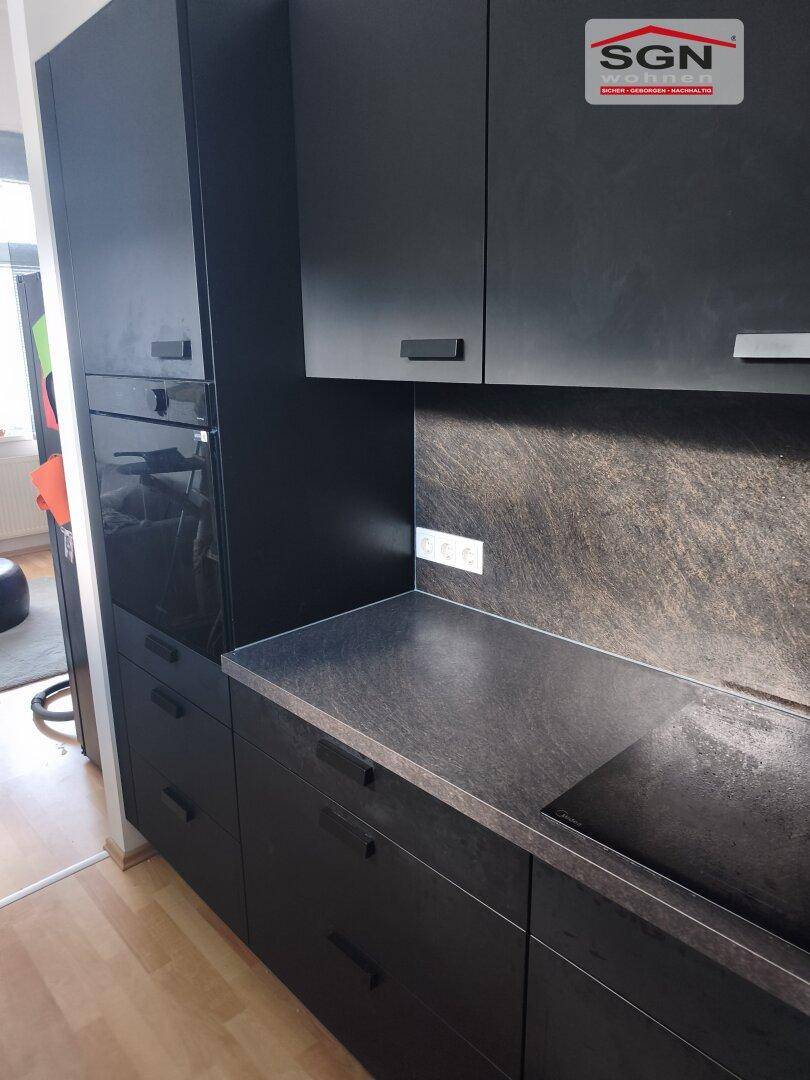Moderne Küche mit schwarzen Schränken, dunkler Arbeitsplatte, integriertem Backofen und Induktionskochfeld.