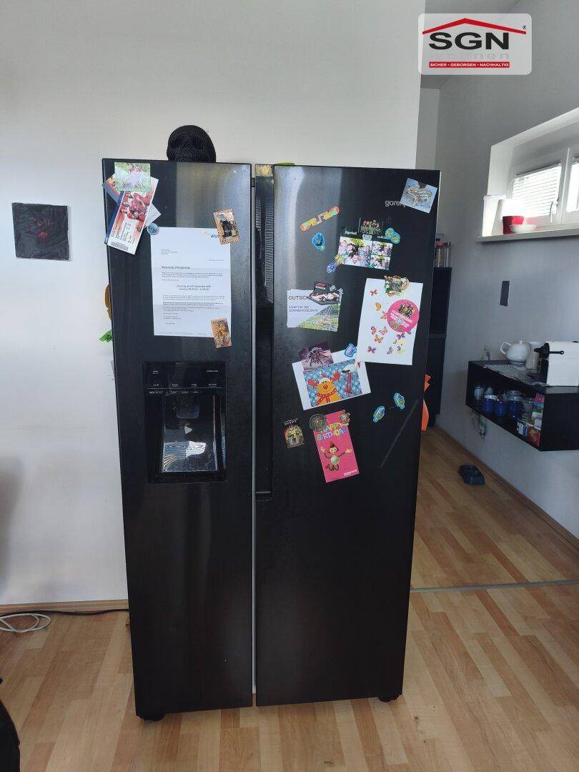 Großer schwarzer Side-by-Side Kühlschrank mit Eismaschine in der Küche auf Laminatboden.