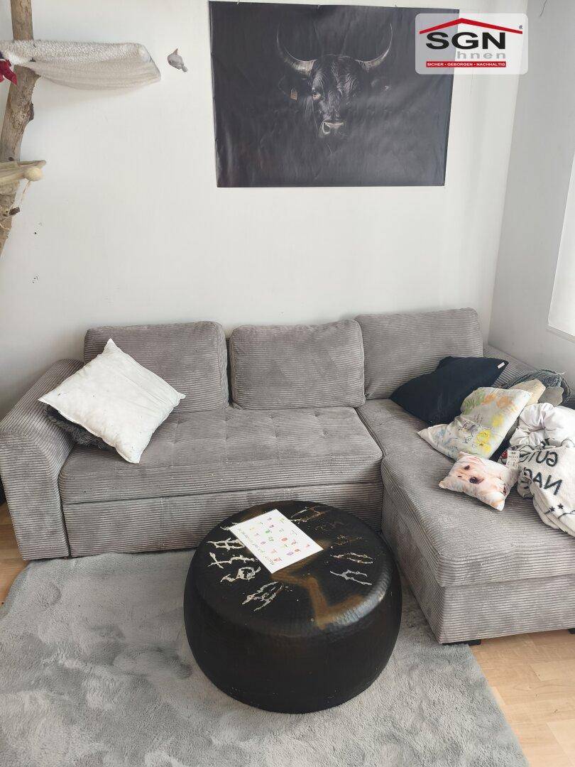 Gemütliches Wohnzimmer mit grauem Ecksofa, rundem Couchtisch und dunklem Wandbild.