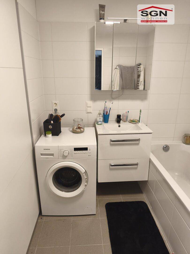 Badezimmer mit Waschmaschine, Waschtisch, Spiegelschrank und einer Badewanne.