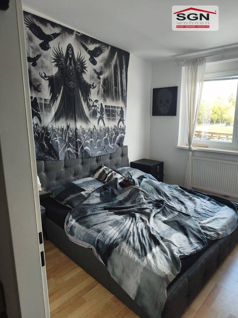 Schlafzimmer mit Doppelbett, dunkler Bettwäsche und großem Wandteppich über dem Bett.