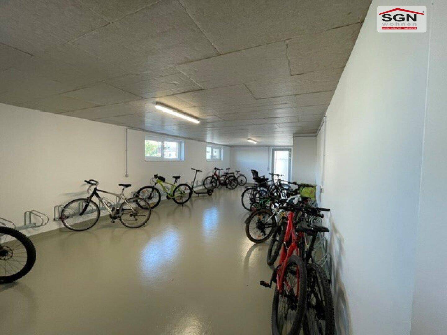 Geräumiger Fahrradraum im Untergeschoss mit zahlreichen Fahrrädern und hellen Wänden.