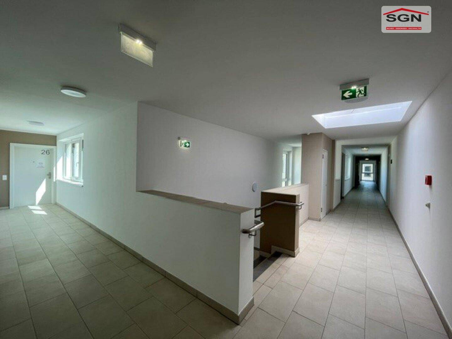 Heller Flur in einem Mehrfamilienhaus mit Fliesenboden, Fenstern und Zugang zu den Wohnungen.