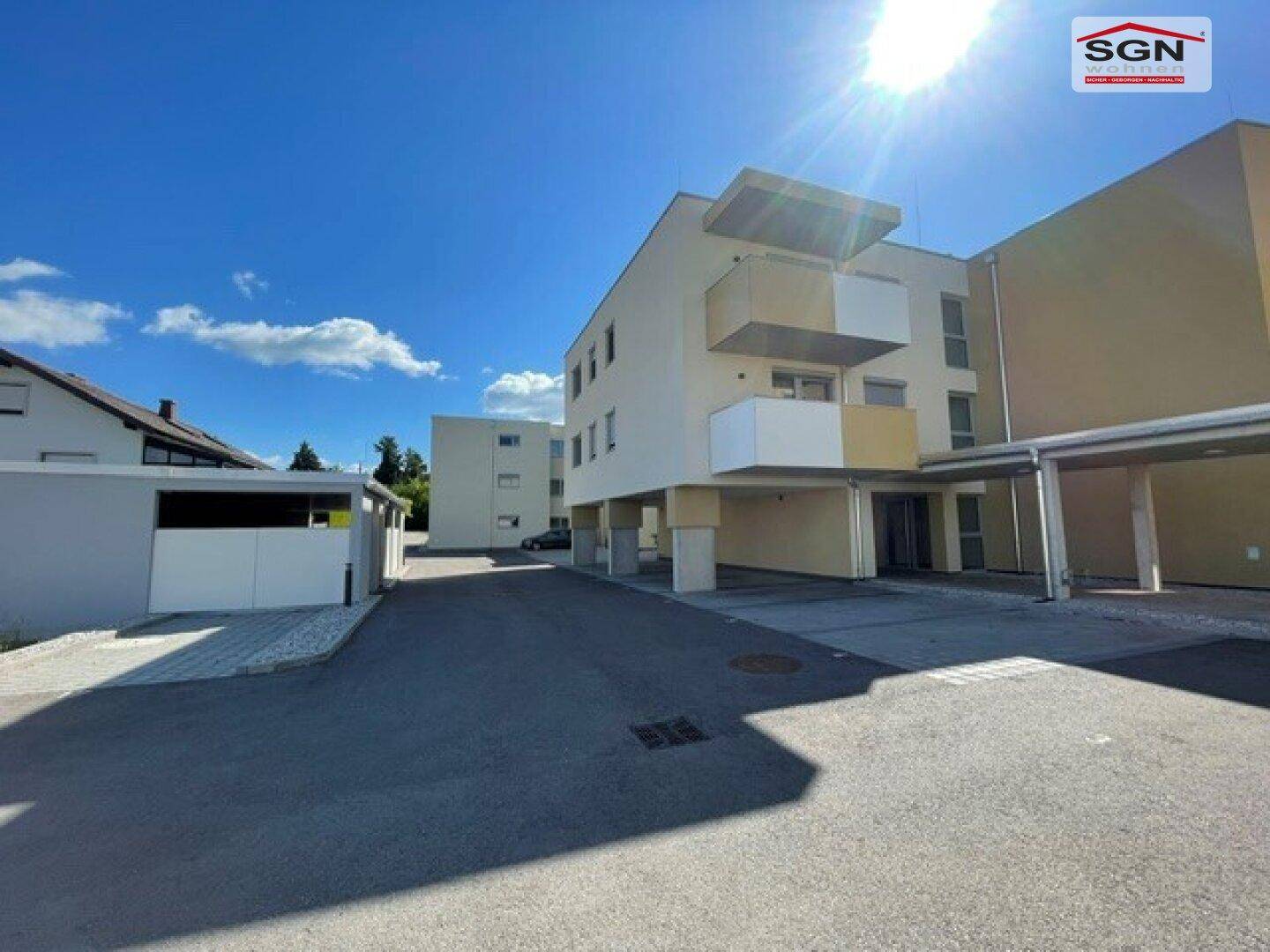 Außenansicht einer modernen Wohnanlage mit Carport und Parkplätzen unter strahlend blauem Himmel.