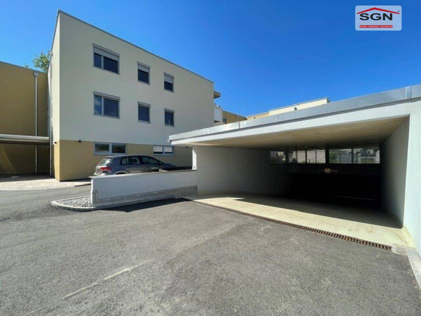 Moderne Wohnanlage mit überdachtem Parkbereich und weiteren Stellplätzen im Freien.