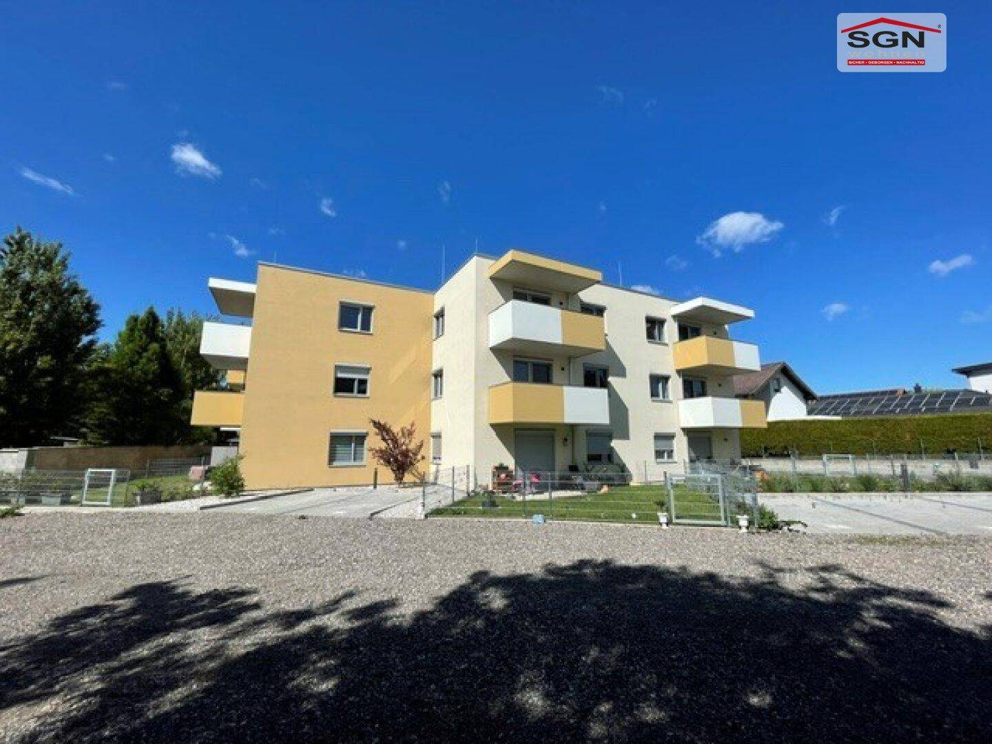 Gesamtansicht einer modernen Wohnanlage mit gelber Fassade, Balkonen und großem Schotterparkplatz.