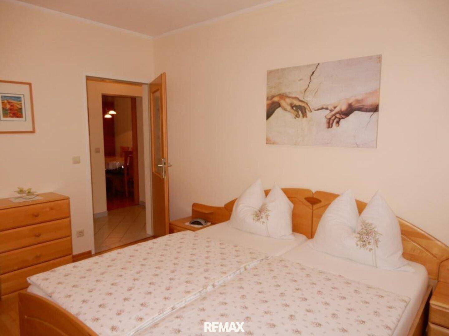 Schlafzimmer mit zwei Einzelbetten, Holzmöbeln und einem Kunstwerk an der Wand.