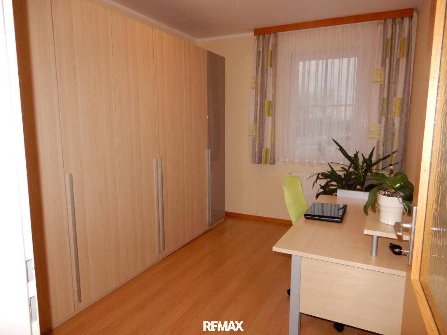 Helles Arbeitszimmer mit großem Einbauschrank, Schreibtisch und Holzboden.