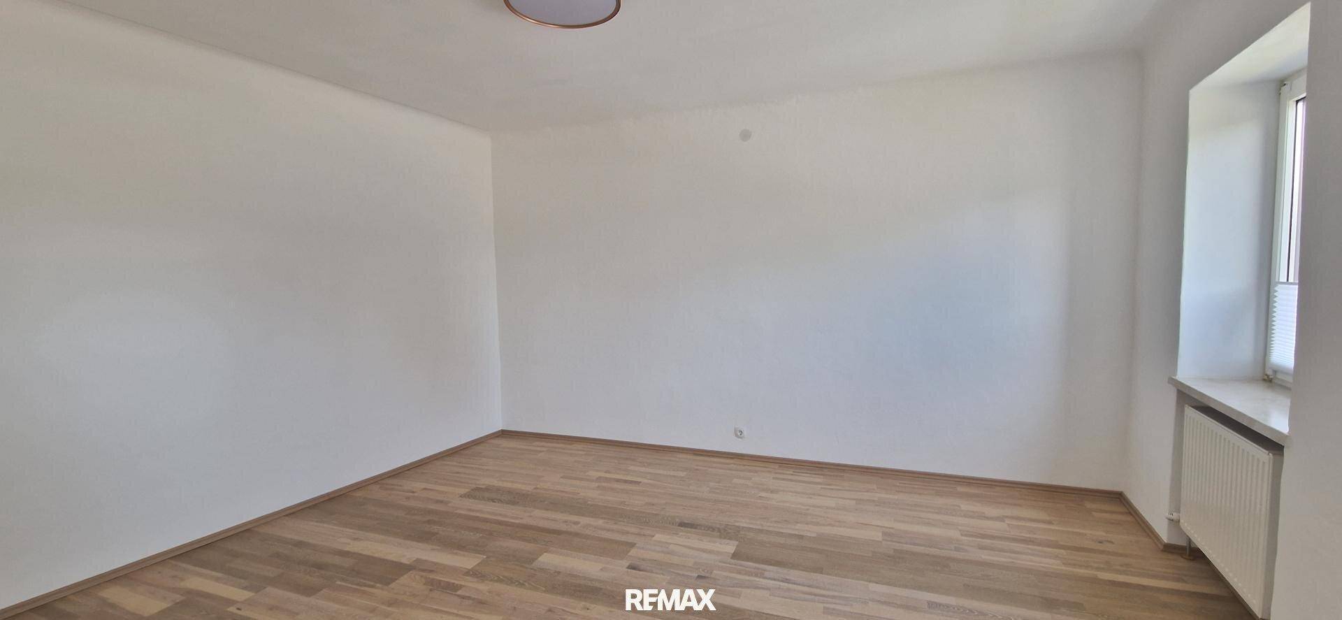 Heller Wohnraum mit Parkettboden und einem Fenster, das viel natürliches Licht hereinlässt.