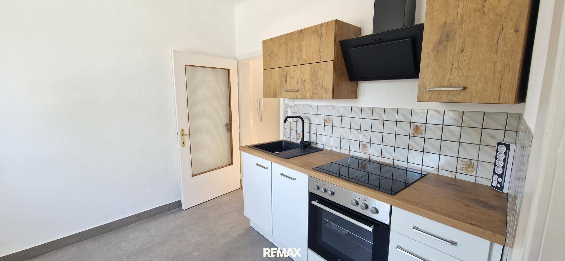 Funktionale Küche mit Holz- und weißen Schränken, Induktionskochfeld und Zugang zu einem weiteren Zimmer.