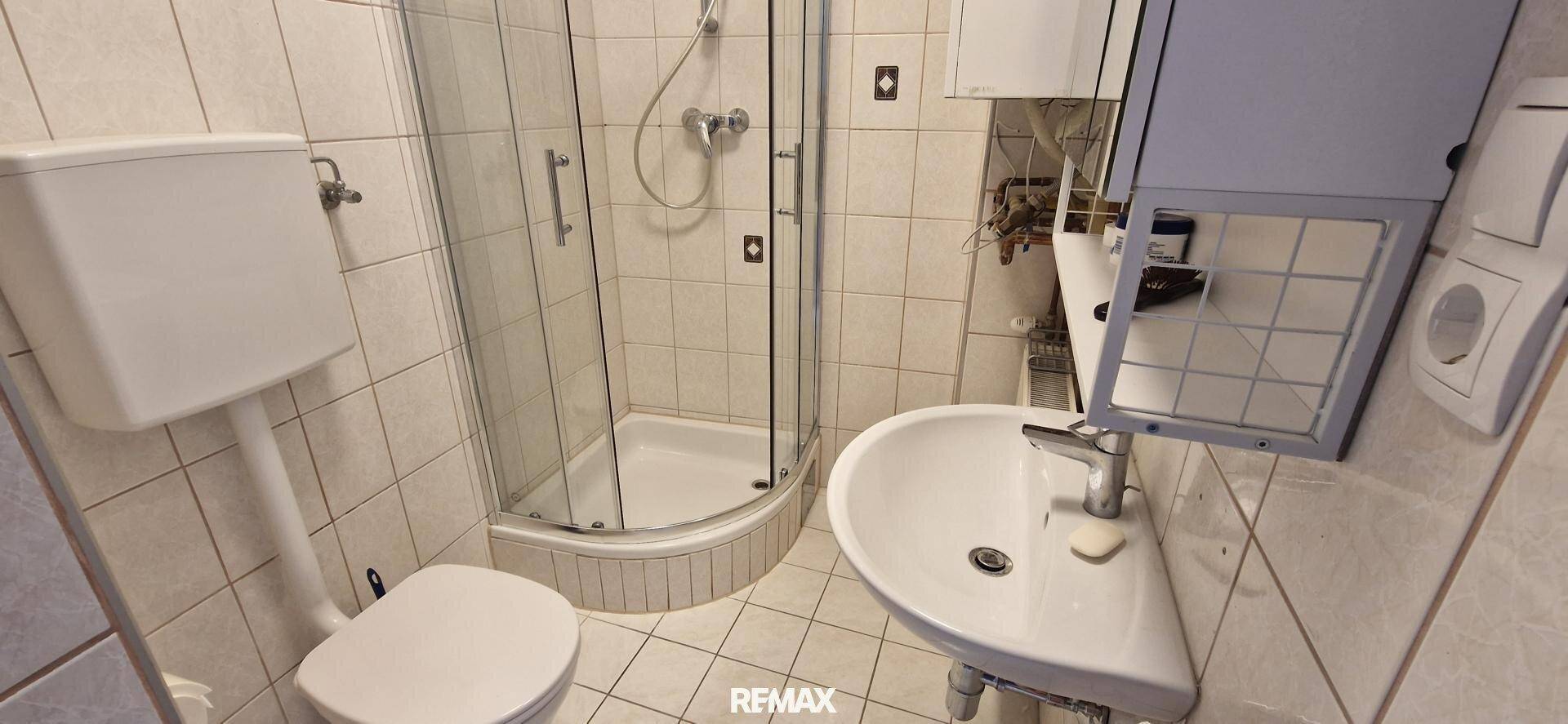 Kleines Badezimmer mit Duschkabine, WC, Waschbecken und Fliesen an Wänden und Boden.