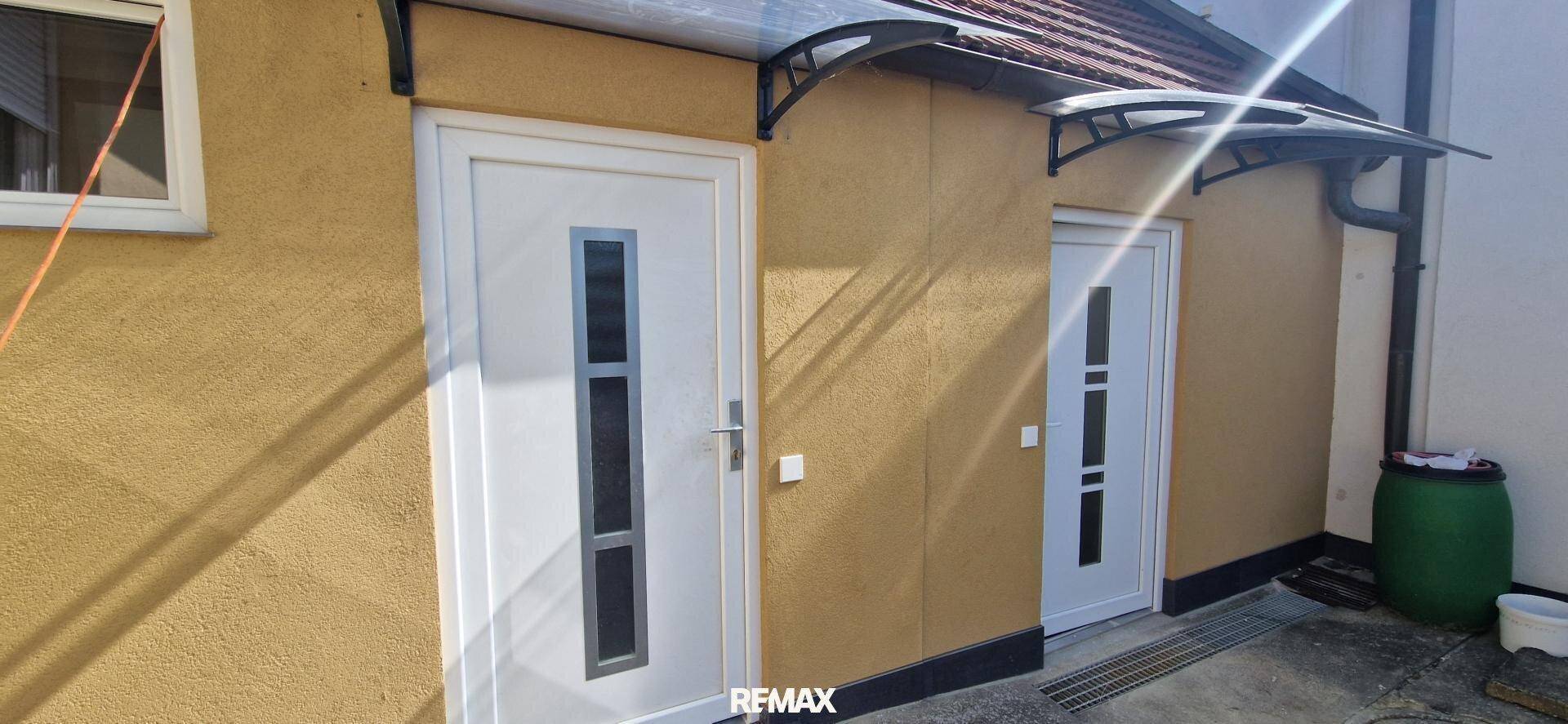 Zwei moderne Eingangstüren mit Vordächern an einer gelb verputzten Hausfassade.