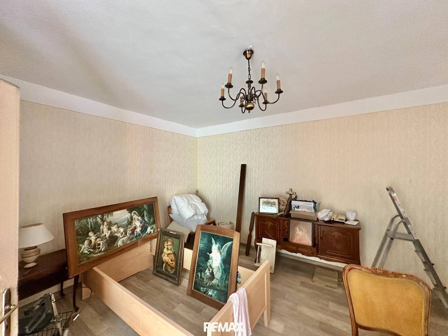 Renovierungsbedürftiges Zimmer mit alter Tapete, Holzboden und Kronleuchter.