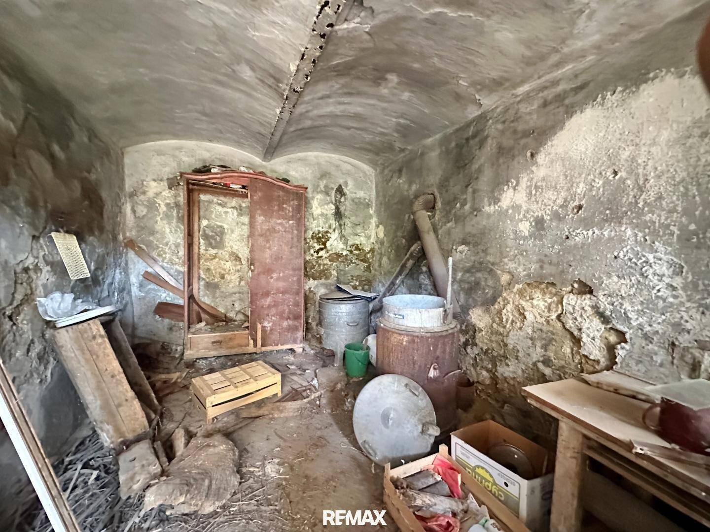 Dunkler Kellerraum mit Steinwänden, gewölbter Decke und verschiedenen alten Gegenständen.