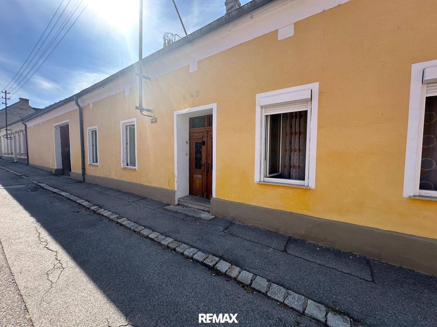 Gelbe Hausfassade an einer ruhigen Straße mit traditionellen Fenstern und Rollläden.
