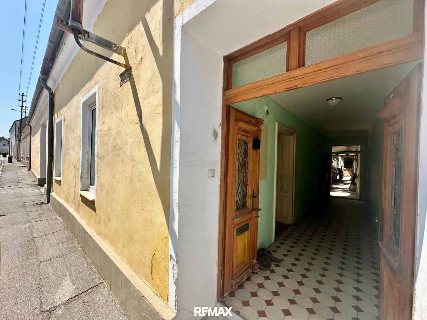 Historische Fassade mit gelbem Putz und einer offenen Holztür, die in einen Flur führt.