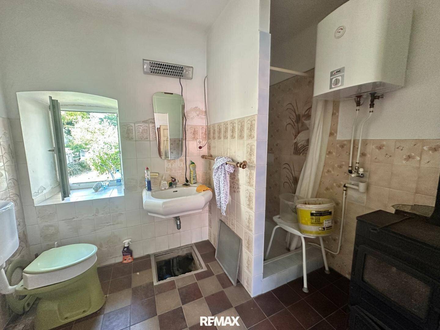 Altes Badezimmer mit Fliesen, Fenster und einem Boiler über der Dusche.
