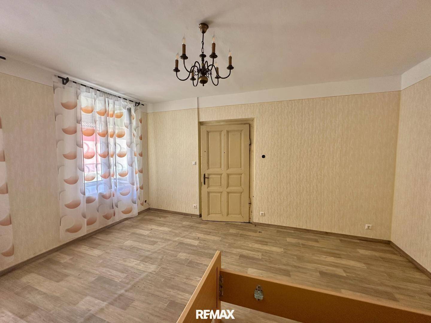 Leeres Schlafzimmer mit gemusterter Tapete, Holzboden und einem Kronleuchter.