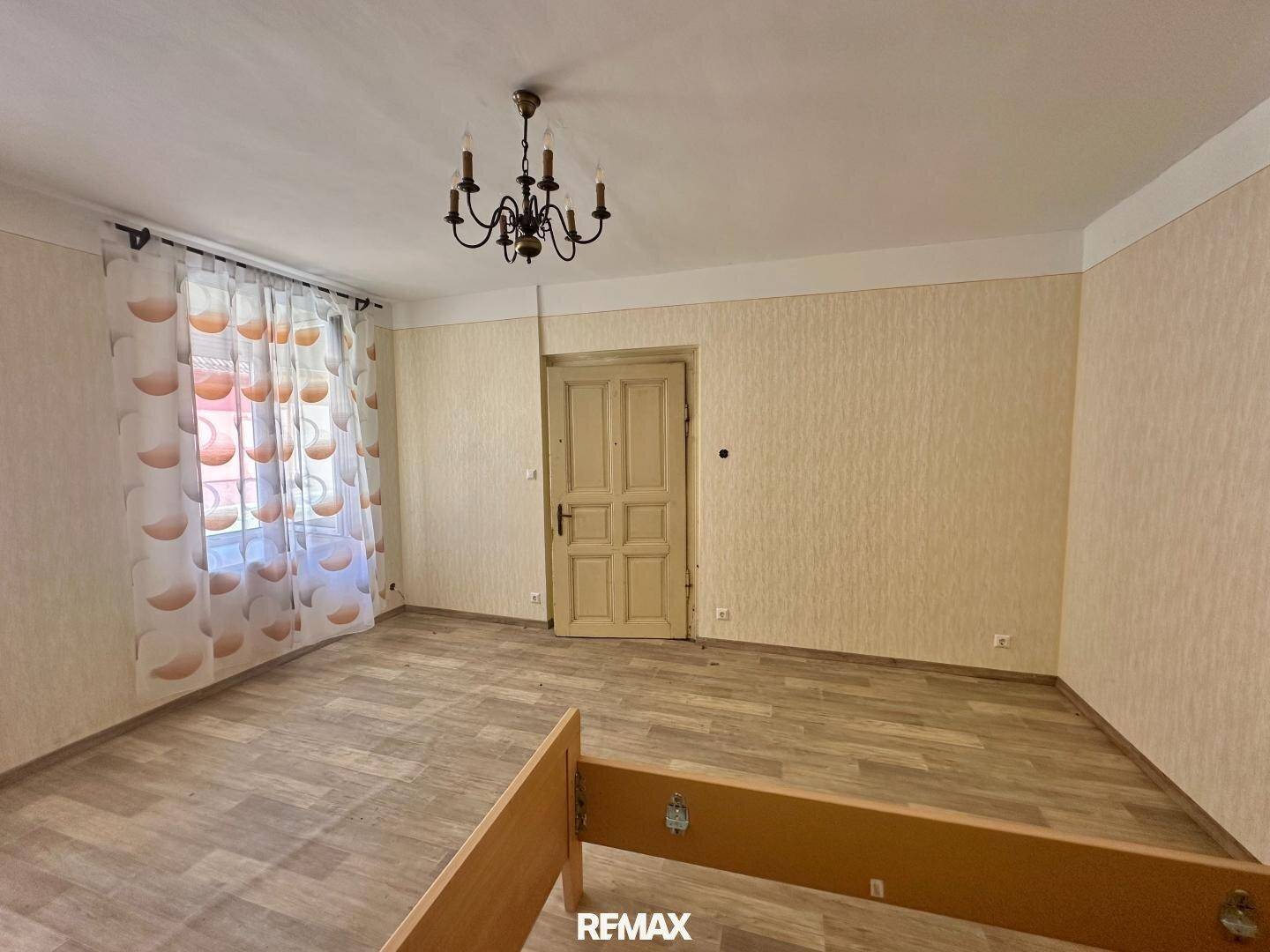 Leeres Schlafzimmer mit gemusterter Tapete, Holzboden und einem Kronleuchter.