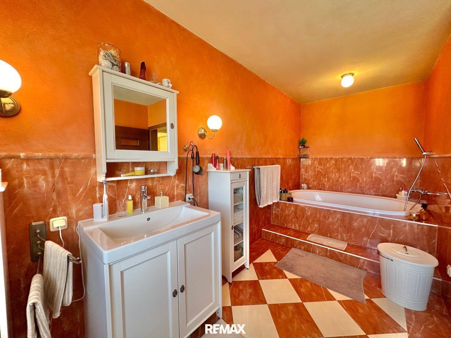 Geräumiges Badezimmer mit auffälligen orangefarbenen Wänden, gemusterten Fliesen und einer Badewanne.
