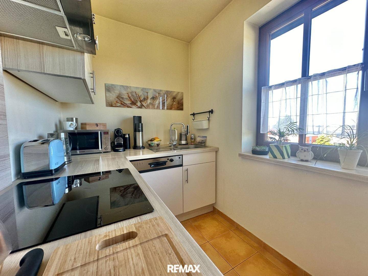 Funktionale Küche mit hellen Holzfronten, Induktionskochfeld und Fenster mit Blick ins Grüne.