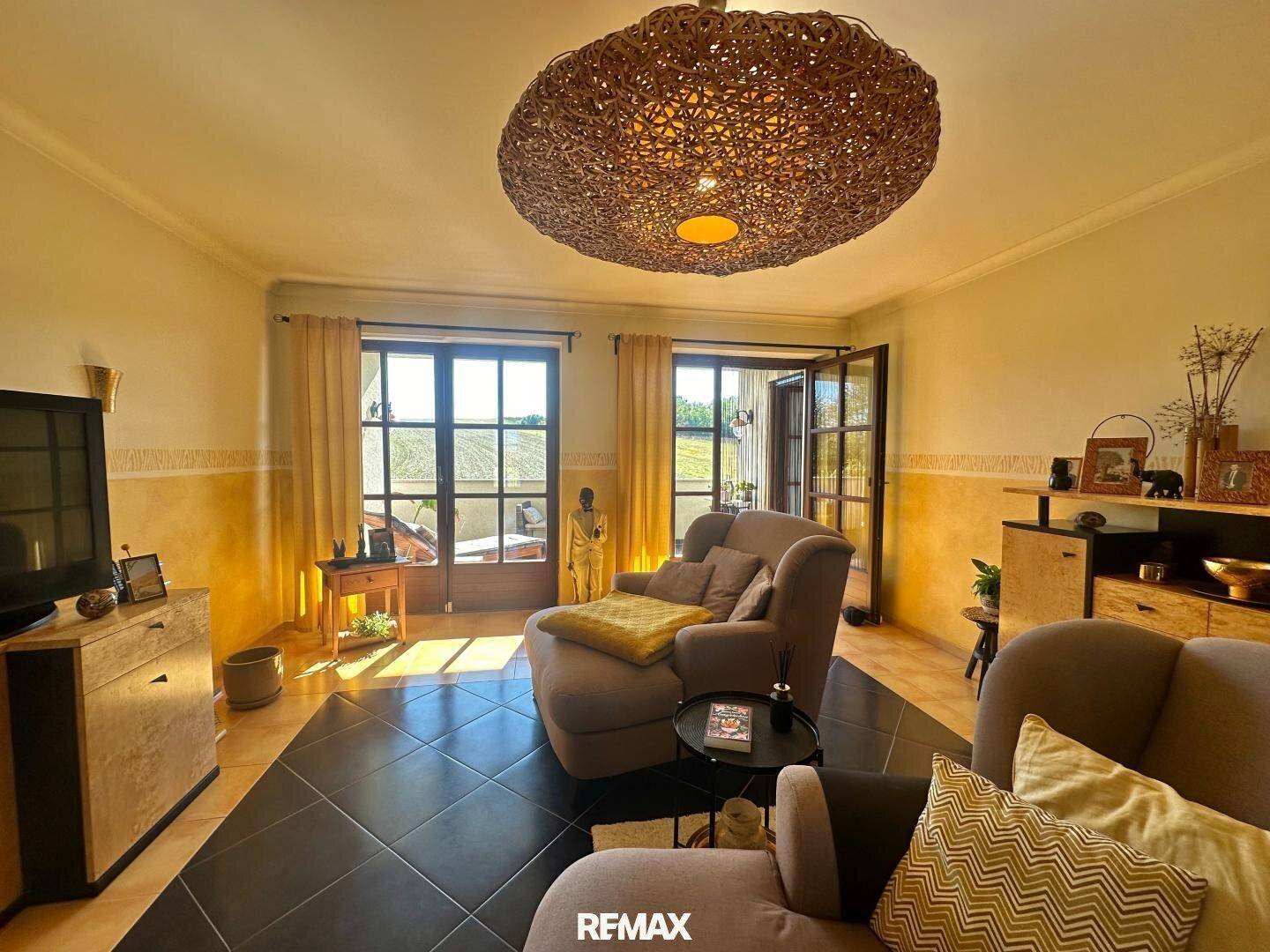 Gemütliches Wohnzimmer mit bequemen Sesseln, dunklen Fliesen und Zugang zu einem Balkon.