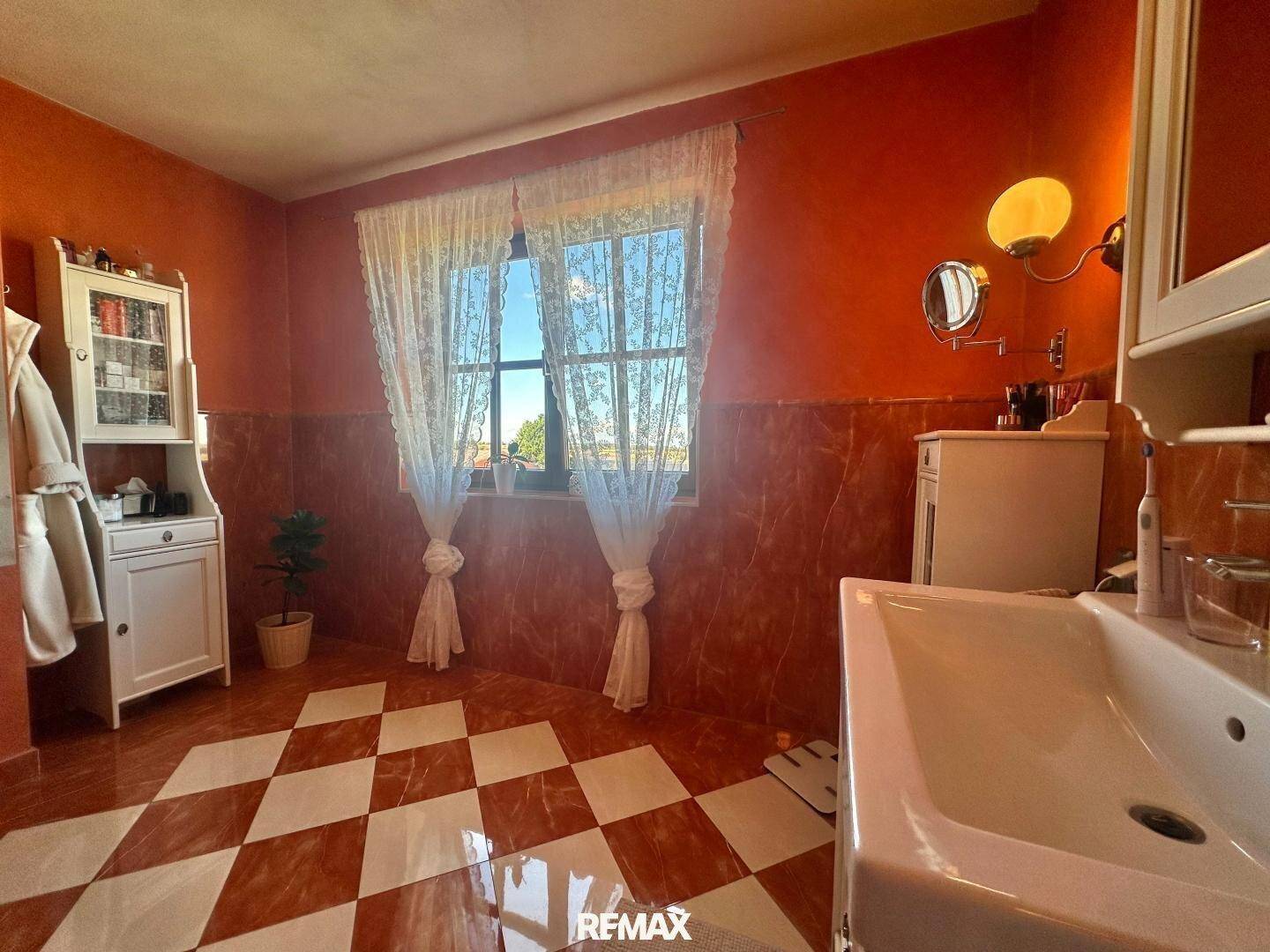 Helles Badezimmer mit Fenster, orangefarbenen Wänden und einem markanten Schachbrettmuster auf dem Boden.