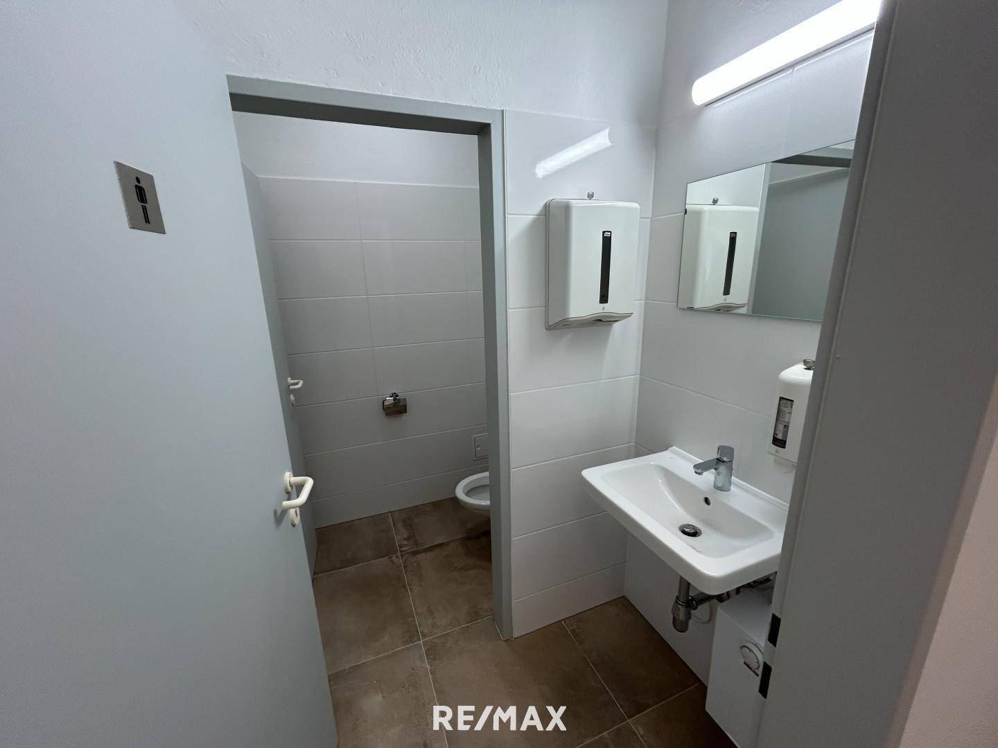 Funktionale Gästetoilette mit Waschbecken, Spiegel und hellen Fliesen, gut gepflegt.