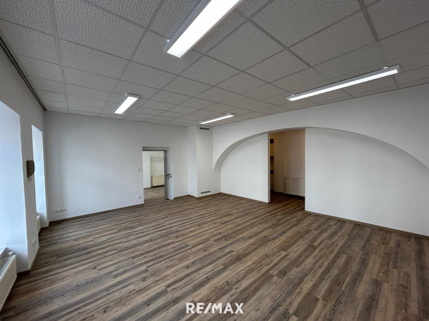Geräumiger Büroraum mit Laminatboden, abgehängter Decke und einem Durchgang zu weiteren Bereichen.