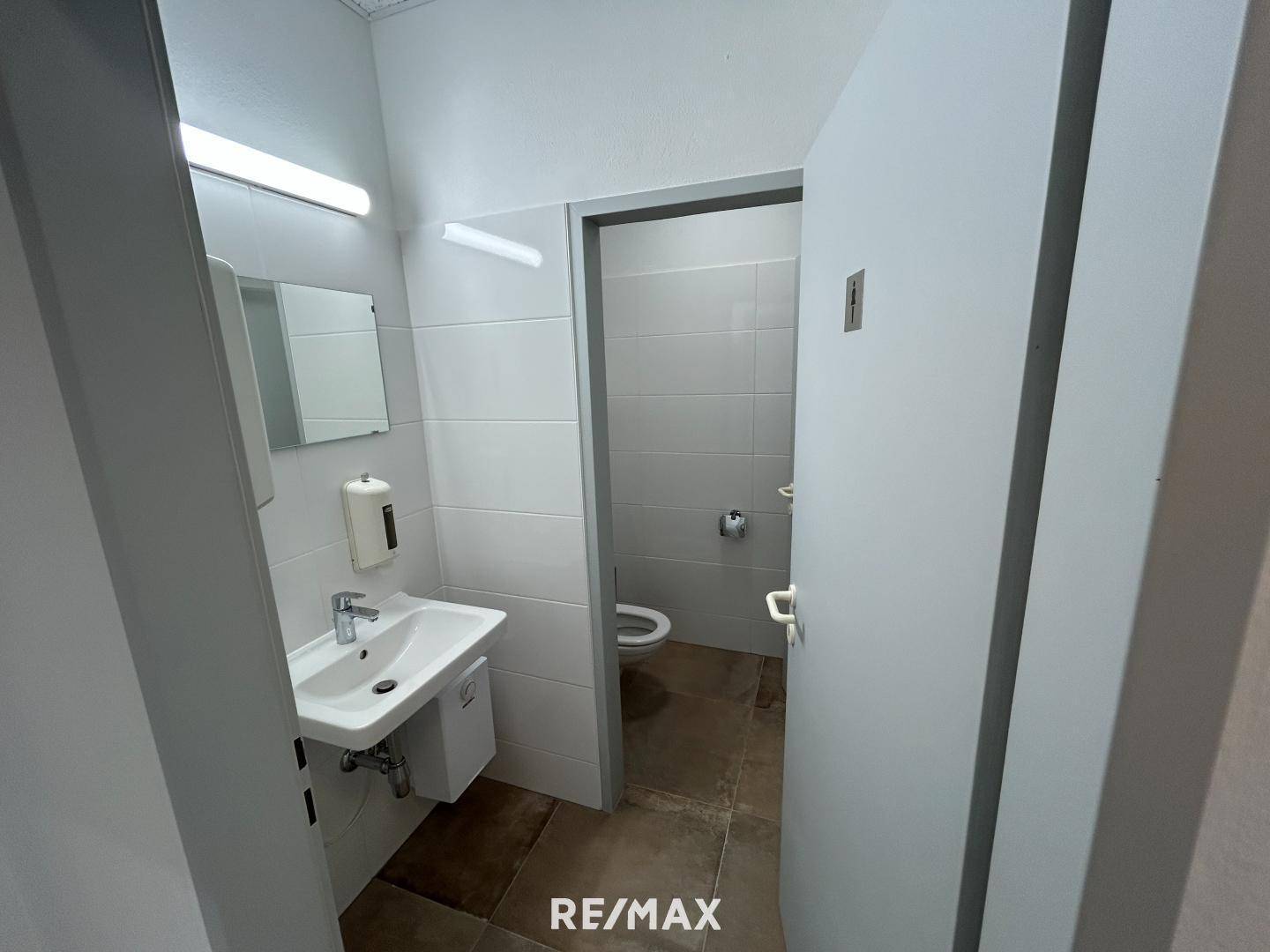 Saubere Gästetoilette mit Waschbecken, Spiegel und Fliesenboden in hellem Design.