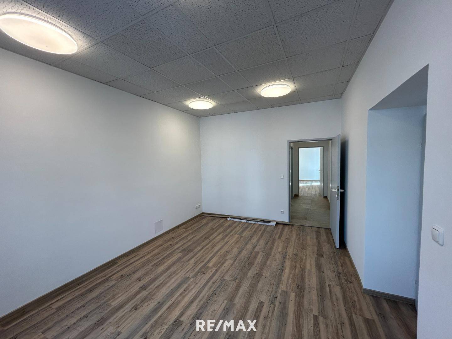Geräumiger Büroraum mit Laminatboden, abgehängter Decke und einem Durchgang zu weiteren Bereichen.
