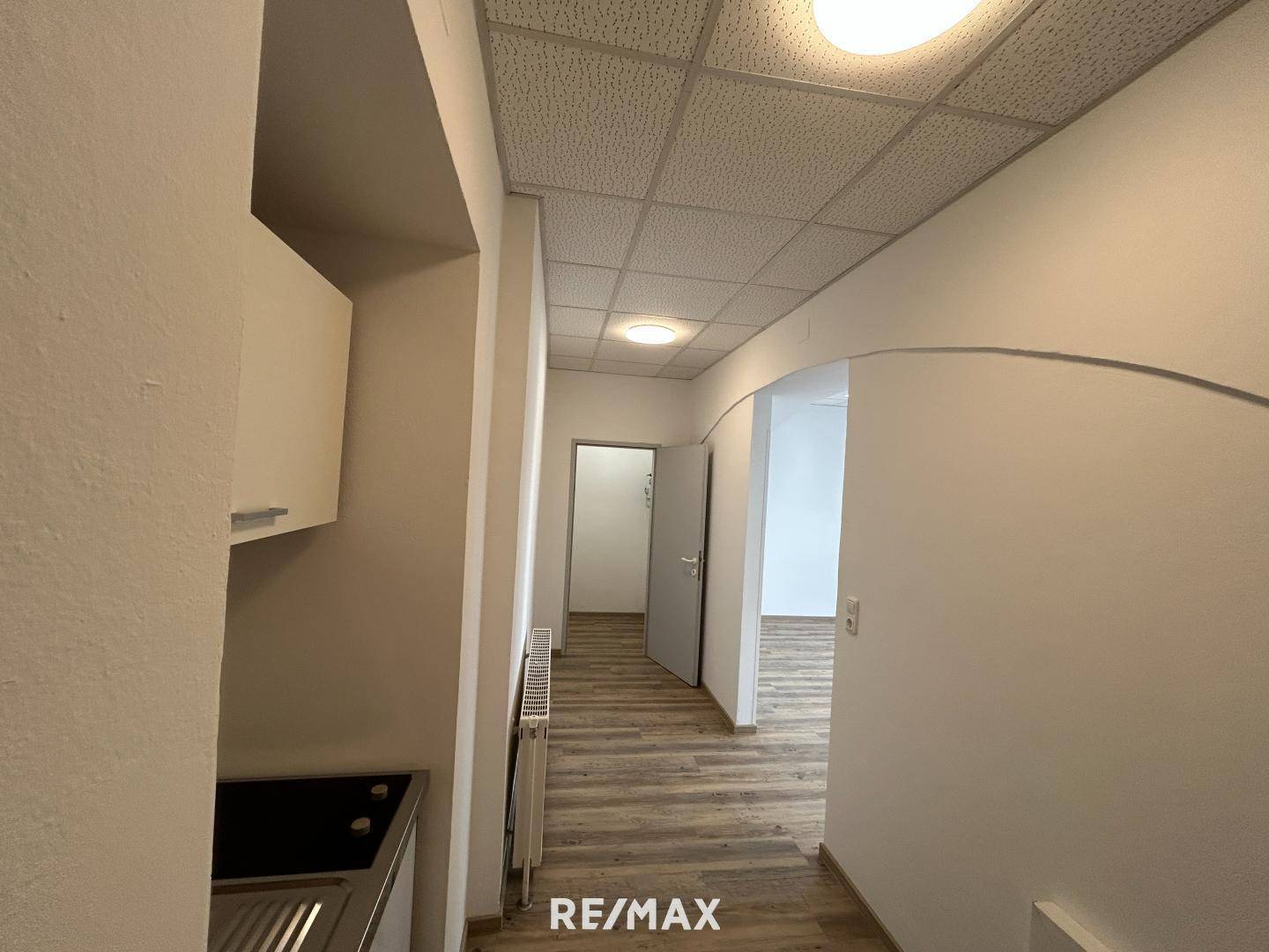 Heller Flur mit Laminatboden, abgehängter Decke und Zugang zu mehreren Räumen.