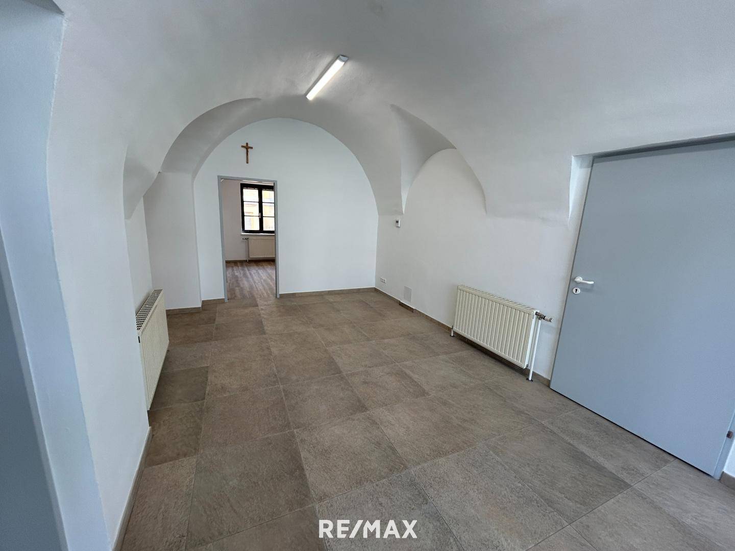 Geräumiger Innenraum mit markanter Gewölbedecke, Fliesenboden und einem Fenster im hinteren Bereich.