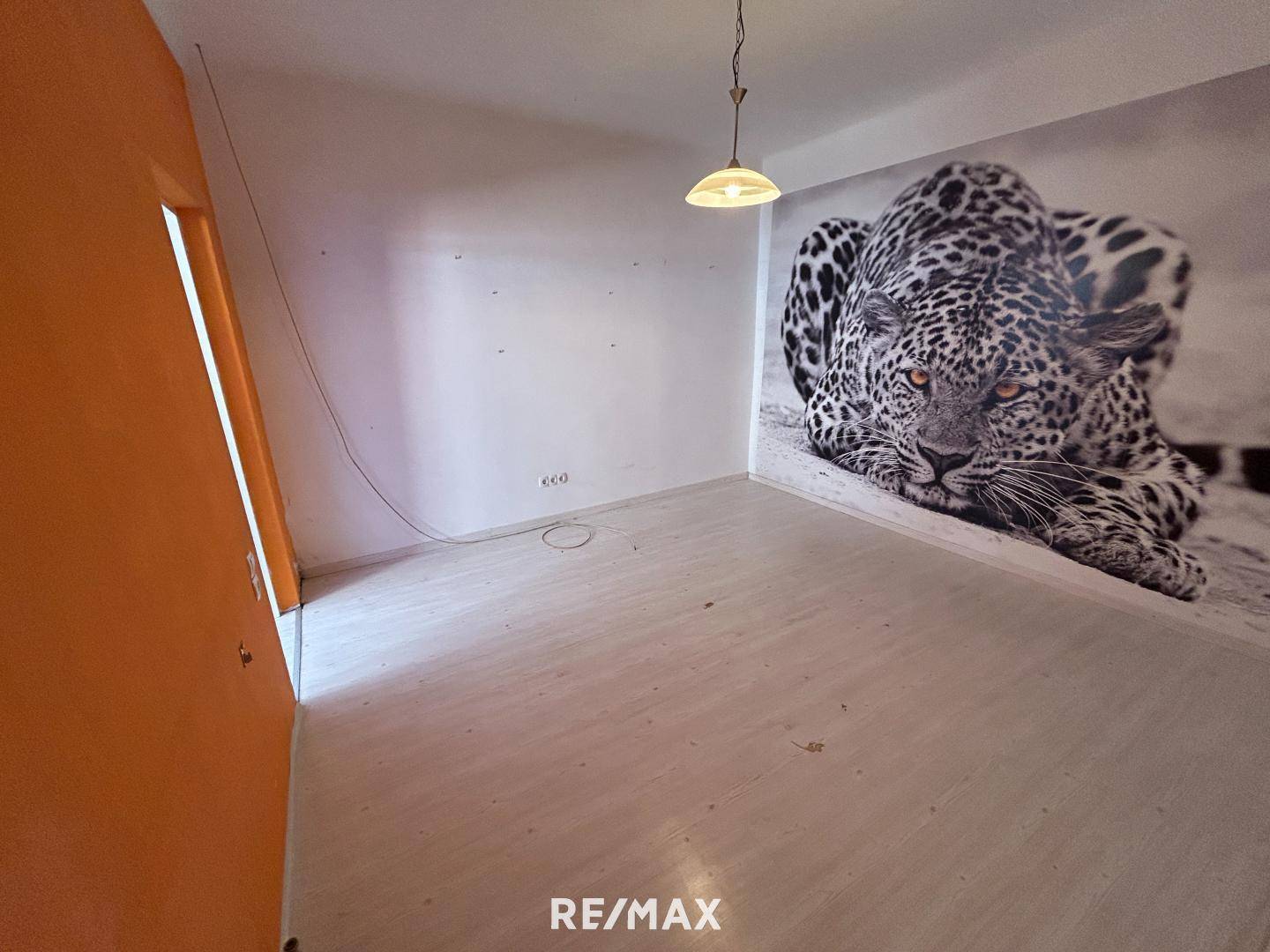 Raum mit hellem Laminatboden und einer auffälligen Wandtapete mit Leopardenmotiv.