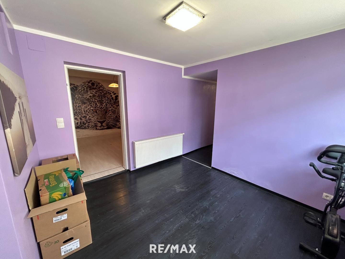 Raum mit lila Wänden, dunklem Boden und einem Heimtrainer, der auf Renovierungsbedarf hindeutet.