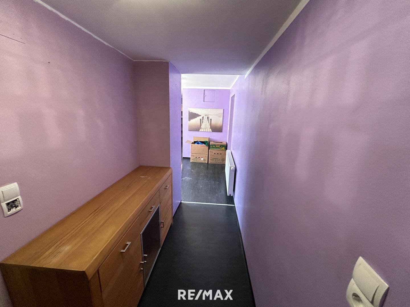 Flur mit lila Wänden, dunklem Boden und einem Holzschrank, der Renovierungsbedarf zeigt.