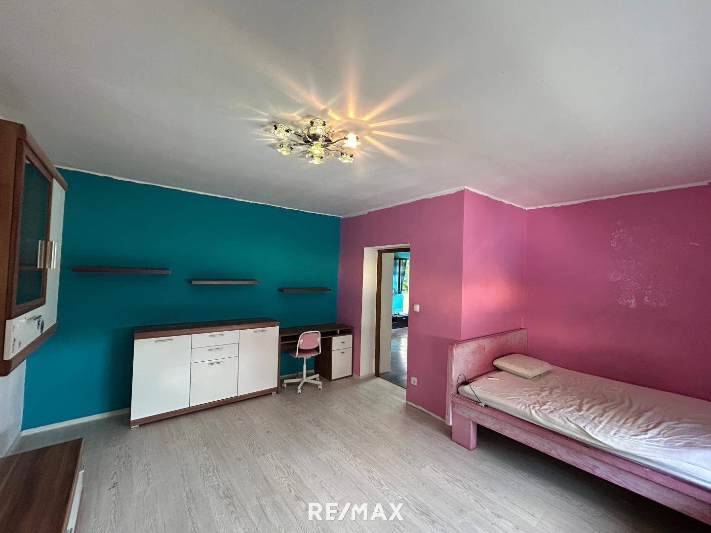 Raum mit farbenfrohen Wänden, hellem Laminatboden und einem Einzelbett.