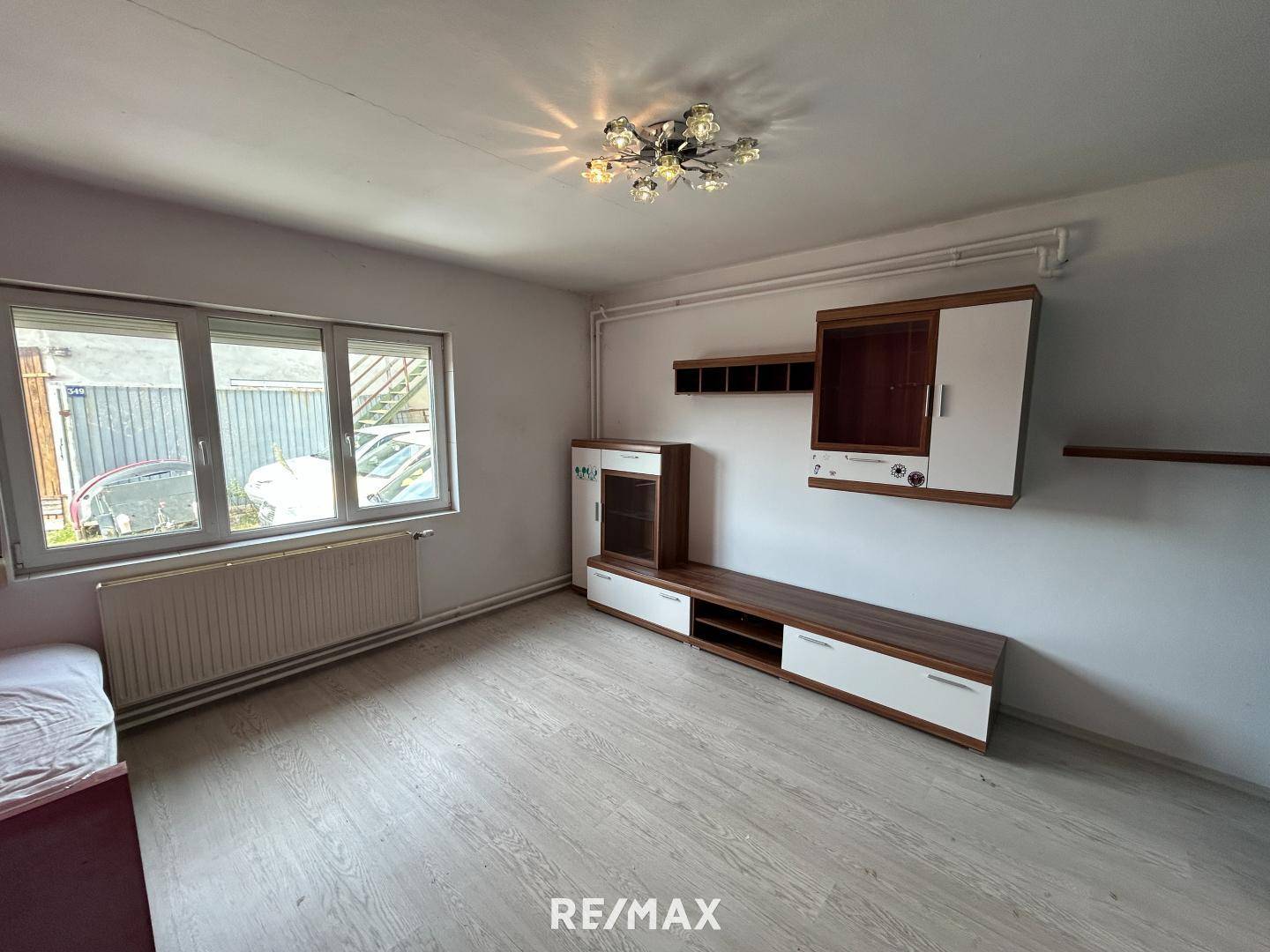 Wohnraum mit hellem Laminatboden, Fenster mit Rollläden und einer modernen Medienwand.