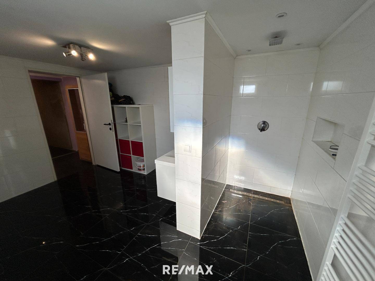 Modernes Badezimmer mit begehbarer Dusche, schwarzen Fliesen in Marmoroptik und weißen Wandfliesen.