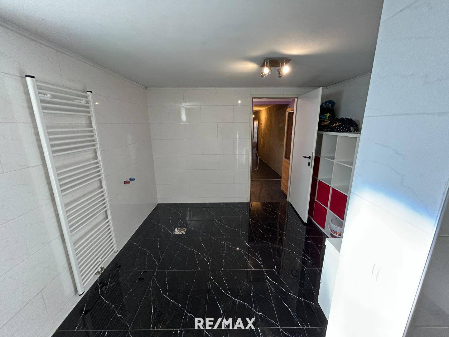 Geräumiges Badezimmer mit schwarzen Fliesen in Marmoroptik, weißen Wandfliesen und Handtuchheizkörper.