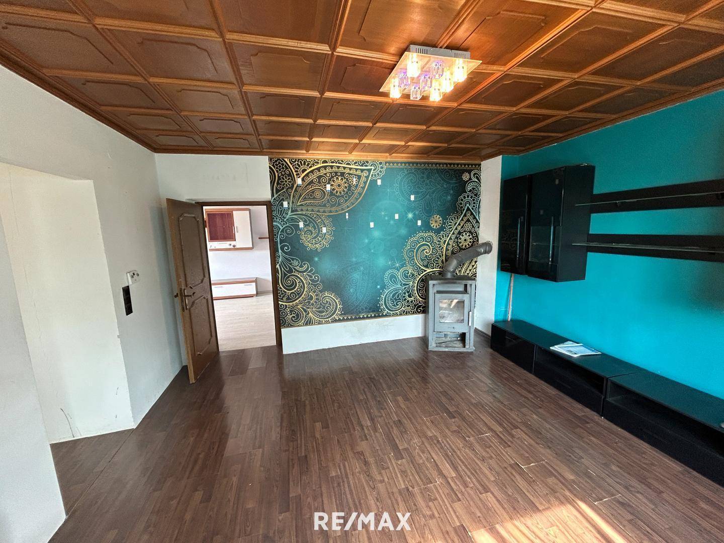 Wohnzimmer mit Holzkassettendecke, dekorativer Tapete und einem gemütlichen Kaminofen.